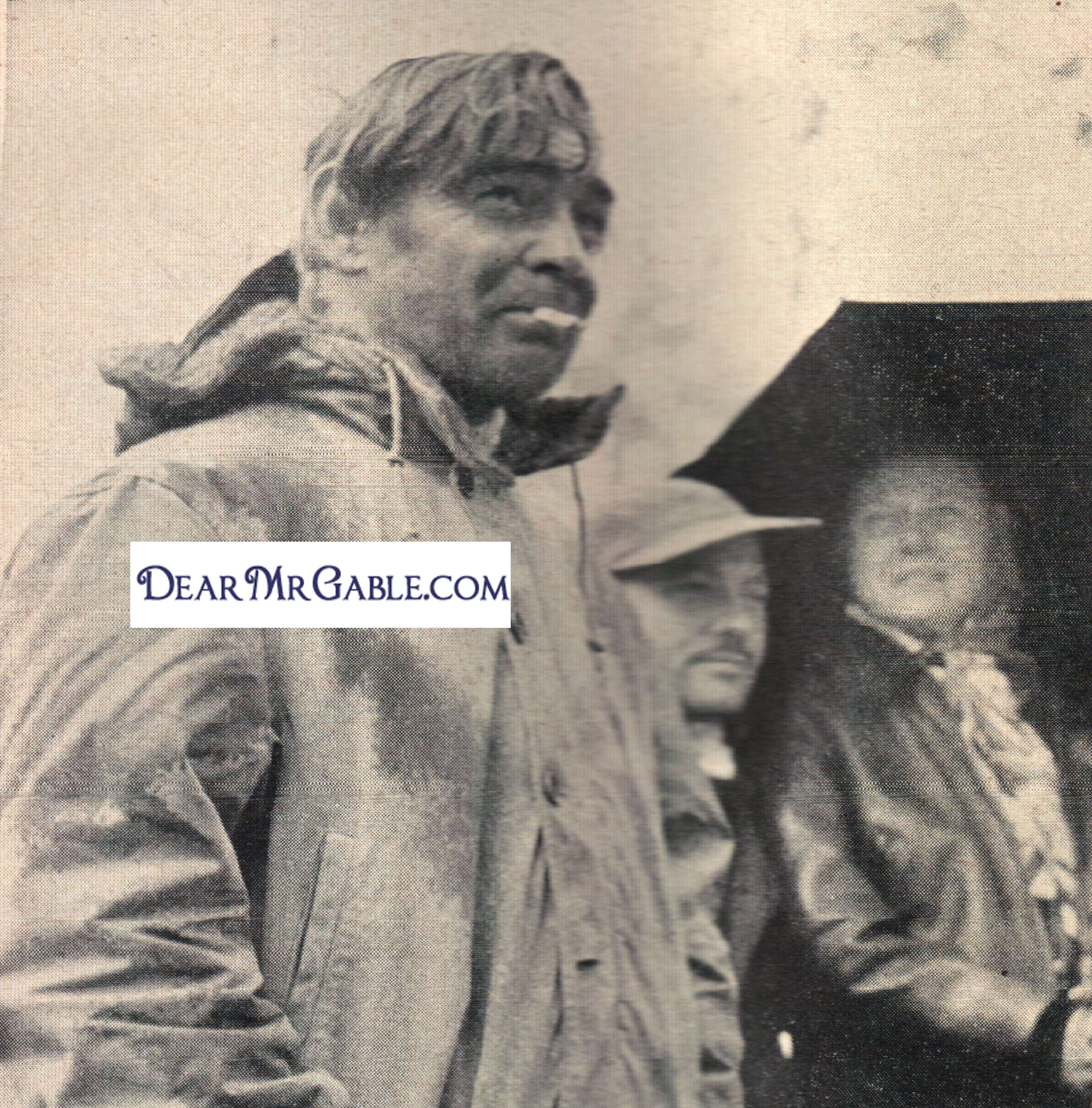 Gable stands out in the rain, waiting for a take, while others take shelter in a tent. The rain is atmosphere for a burial scene.